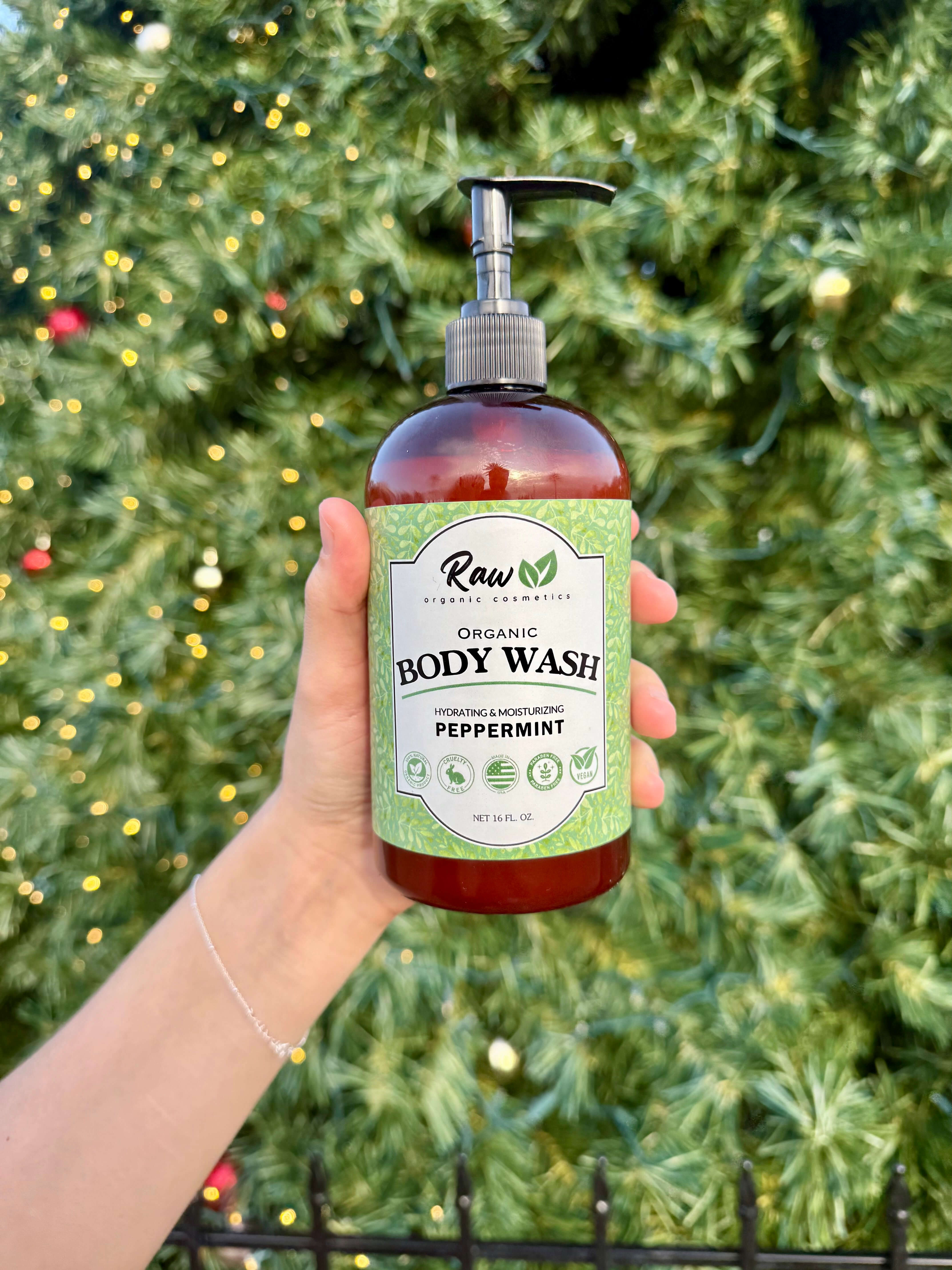Woman holding Raw Organic Cosmetics peppermint body wash in front of a Christmas tree, showcasing it as the perfect holiday gift for refreshing and nourishing skincare